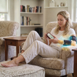 Woman using NYP Nico portable PEMF wellness device on her arm while relaxing in a chair.